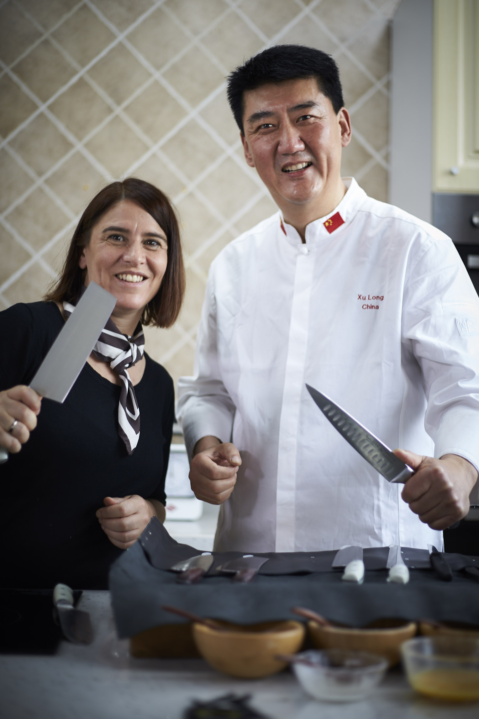 Esther Kern und Chinas Staatskoch Xu Long halten Messer in die Kamera.